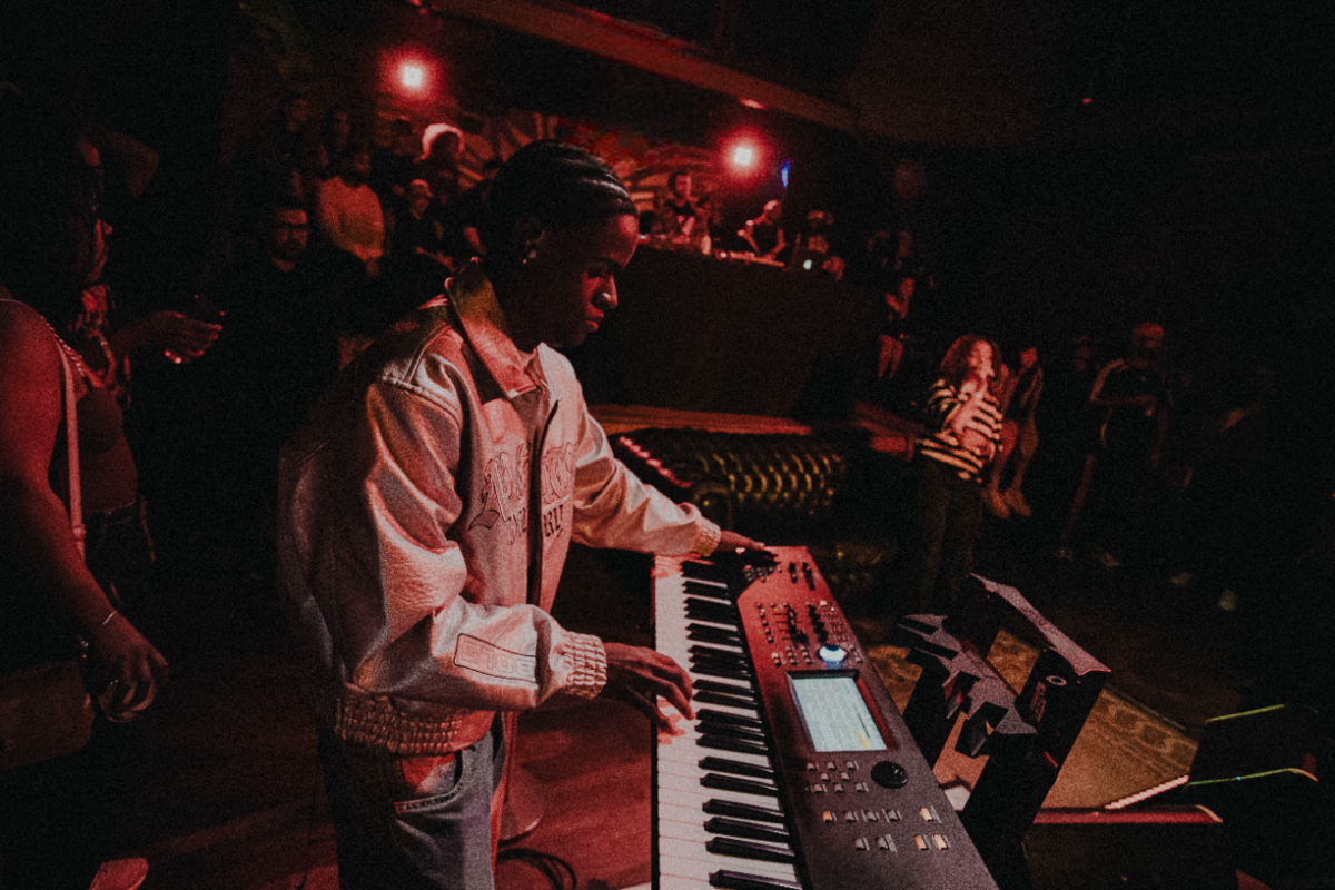 Músico tocando teclado durante sessão com iluminação baixa e foco no instrumento